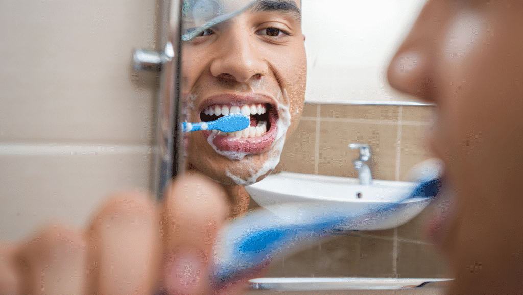 Persona cepillándose los dientes frente al espejo, destacando una dentadura alineada que facilita la limpieza.