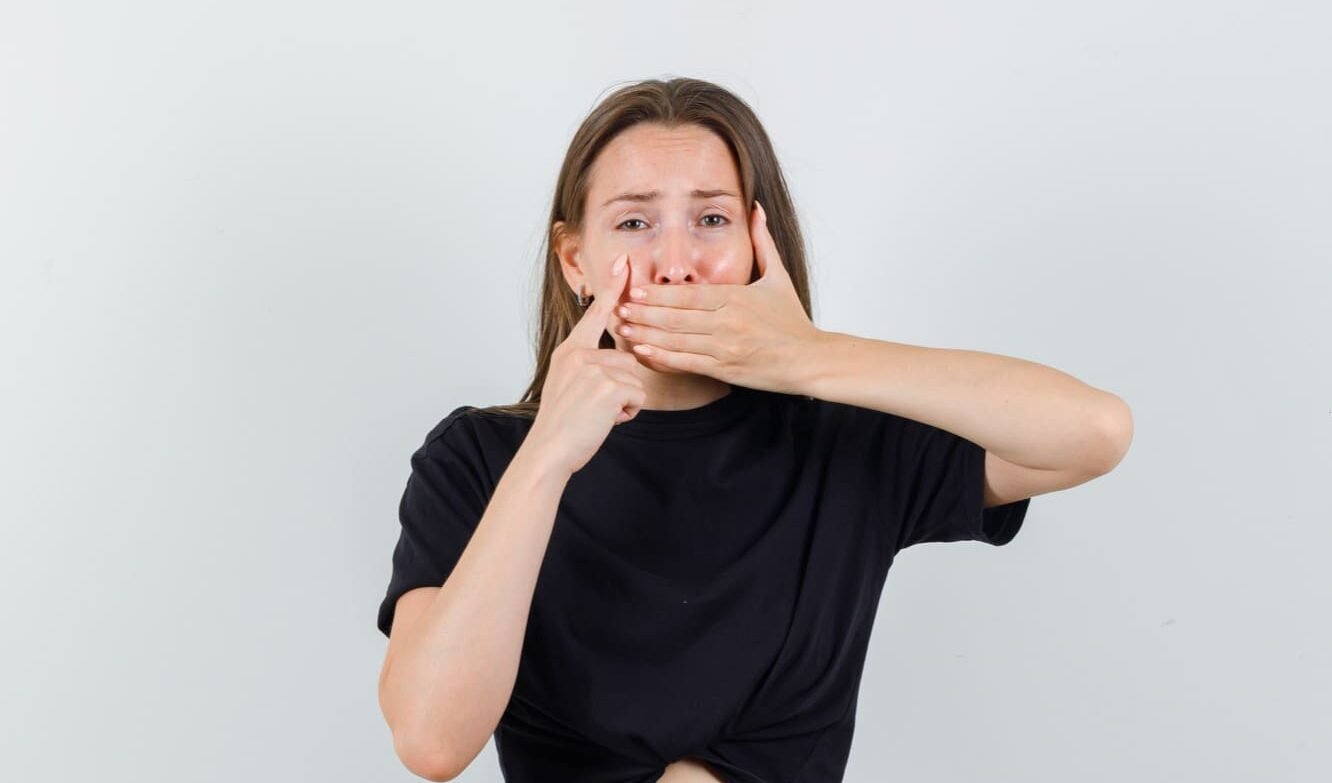 Tapandose la boca con incomodidad