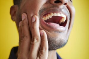 Hombre con dolor de mandíbula sujetándose la cara al abrir la boca